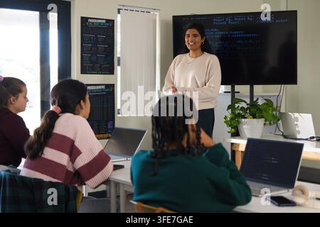 Female teacher leading code class in light sweater with laptops and screen showing code, copy space Stock Photo