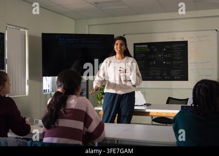 Indian instructor presenting code lesson in room while youth female students sitting with monitor Stock Photo