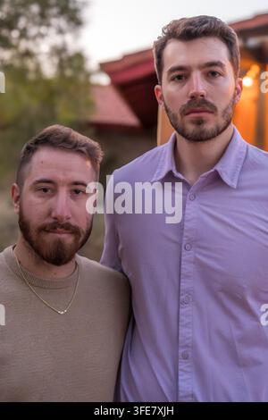 Autumn 2024: Two bearded men in casual sweaters stand close together for a serious outdoor portrait at dusk. Stock Photo