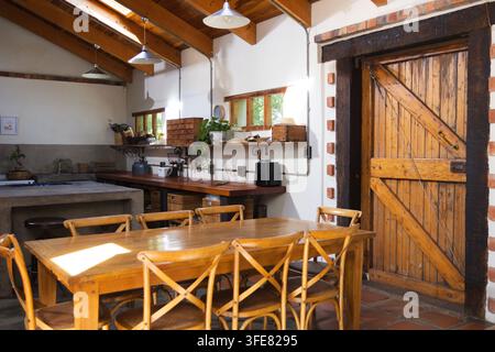 Wooden dining table with six crossback chairs is sitting in sunlit rustic kitchen Stock Photo