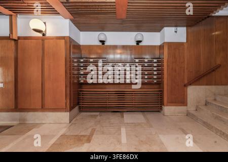 Vintage building entryway featuring built-in wooden mailboxes, marble flooring, and a staircase with a wood handrail. Stock Photo
