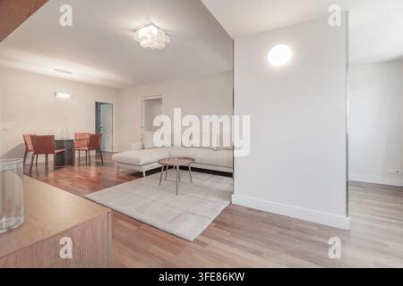 Living room with white sectional sofa, round coffee table, area rug, and dining area with red chairs. Stock Photo