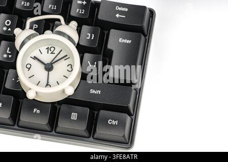 White alarm clock on black keyboard near enter key, symbolizing time pressure and online deadlines. Stock Photo