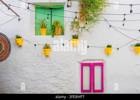 Bright yellow flowerpots, string lights, and a pink window frame set against a whitewashed textured wall in Peñíscola. Stock Photo