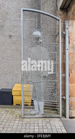 A vertical, full shot captures a decorative, galvanized steel gate featuring an intricate silhouette of a vintage fireman. Stock Photo