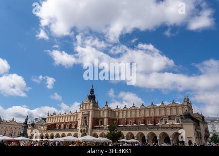 Krakow, Poland - 29.08.2026 Historic market square building rises above crowd under bright blue sky and drifting clouds in Krakow. Arched facade, towe Stock Photo