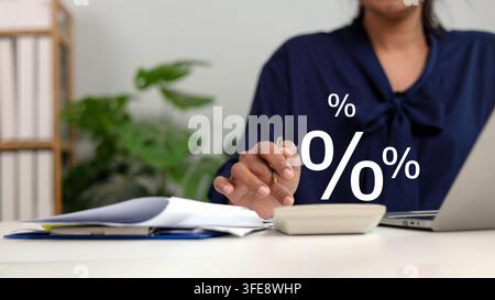 Businesswoman holding pen using calculator with percentage symbol graphic icons overlay. Female accountant analyzing interest rate  tax rate or financ Stock Photo