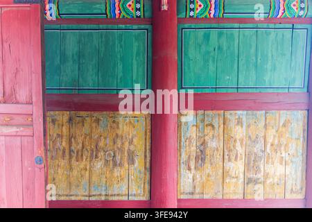 A weathered wooden door and timber facade feature red beams, green panels, and ornate multicolored painted motifs. Stock Photo