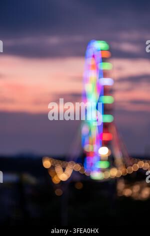 Blurred ferris wheel glowing with rainbow lights at dusk at Nürburgring, evoking a festive, dreamy mood. Stock Photo