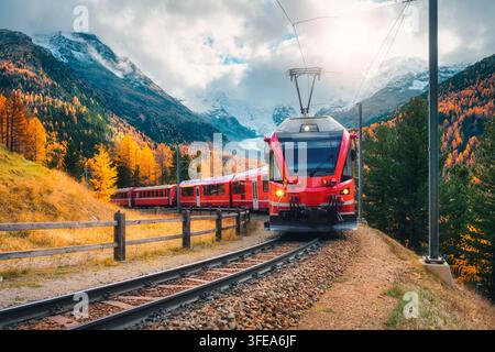 Red modern electric train traveling along a railway in mountains Stock Photo