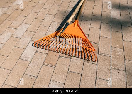 Orange plastic lawn leaf rake lying on stone paved walkway outdoors Stock Photo