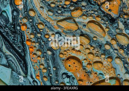 Abstract fluid art macro texture showing orange, grey, and blue paint swirls with oil drops Stock Photo