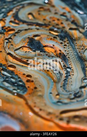 Vertical macro shot of swirling orange, light blue, and black paint with clear oil cell bubbles Stock Photo