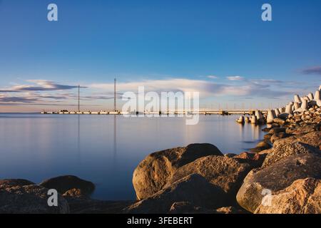 Rocky Coastline and Long Pier at Calm Sea During Golden Hour Stock Photo