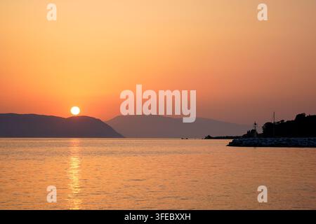 Sun Setting Behind Hills Over a Calm Sea Stock Photo