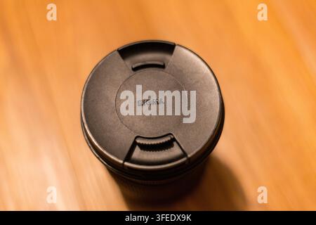 Top-down view of a black camera lens cap resting on a smooth wooden table surface with warm lighting. Stock Photo