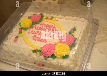 A rectangular anniversary sheet cake decorated with pink and yellow icing roses in a clear plastic container, featuring the text Happy Anniversary Lau Stock Photo
