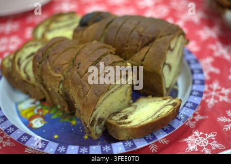 Sliced chocolate swirl babka sweet bread served on a festive Christmas plate on a red snowflake tablecloth. Stock Photo