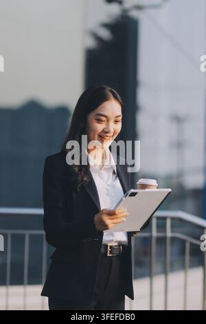 Business woman checks phone in front of modern building during the day Stock Photo