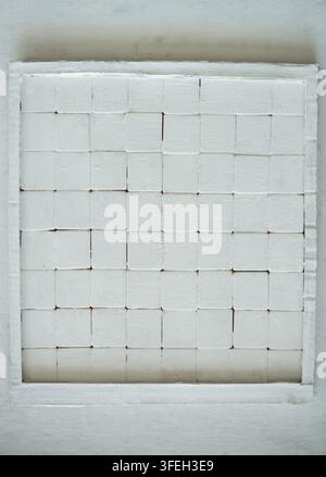 Close-up of a white painted grid of square wooden blocks forming a minimal geometric textured surface and abstract background Stock Photo