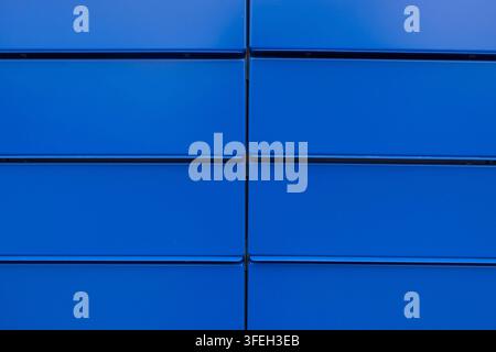 Close-up of bright blue metal wall panels in a regular grid, creating a bold geometric industrial texture and abstract background Stock Photo