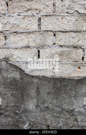 weathered masonry wall with pale bricks, damaged mortar and cracked gray render, showing decay, repair and aged building texture Stock Photo