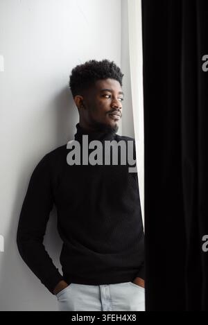 Young Black man in a black turtleneck sweater looking out a window Stock Photo