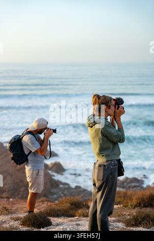 Man and woman taking photos on a cliff by the sea Stock Photo