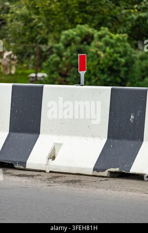 Heavy duty concrete median traffic barrier painted in high-contrast black and white stripes with a red safety reflector on top. Stock Photo