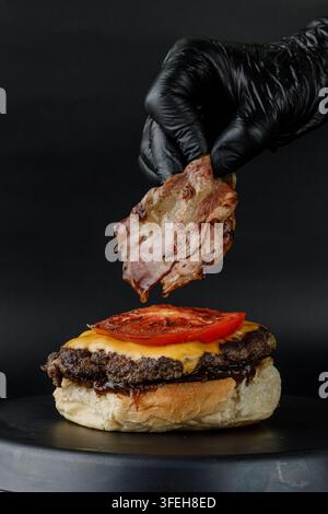 Gloved hand carefully placing bacon on a burger Stock Photo