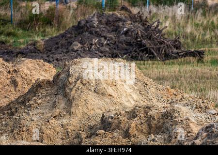 Close view of a fresh excavated yellow soil pile with dark root debris piled up in the background of a building plot. Stock Photo