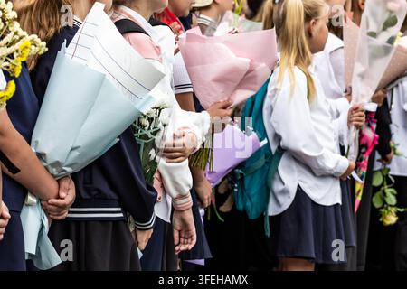 Close-up of school students in dark blue uniforms holding beautiful wrapped flower bouquets behind their backs at a back to school ceremony. Stock Photo