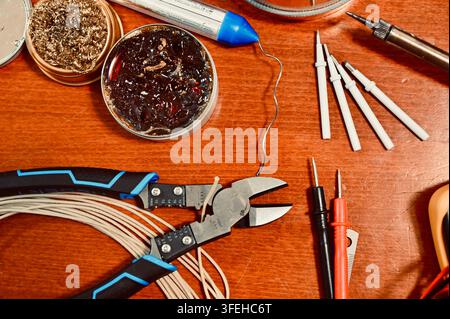 Close-up of electronics and DIY tools on a workbench, featuring wire cutters, copper tape with solder, flux, soldering iron tips, multimeter probes, a Stock Photo