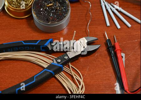 Close-up of electronics DIY tools on a workbench, featuring wire coils, wire cutters, a soldering iron, a multimeter with probes, flux, solder, and a Stock Photo