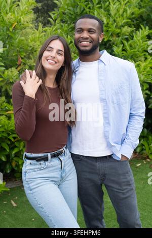 A happy young couple stand close together outdoors, smiling and embracing in a lush green garden, conveying affection, comfort, relaxed lifestyle and Stock Photo