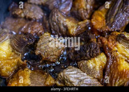 Close-up view of braising beef meat in a pan. Varied textures of meat pieces, with caramelized edges and steam rising, indicate active cooking. Stock Photo