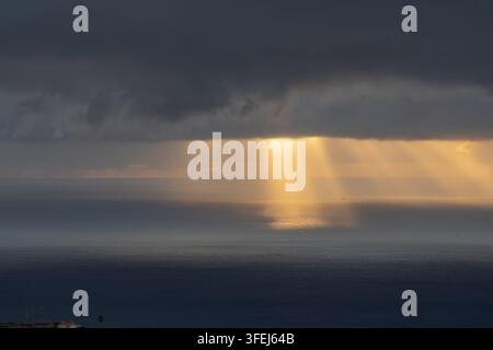 A dramatic dawn over Madeira shows golden sunlight streaming through heavy clouds and reflecting across the calm surface of the Atlantic Ocean. Stock Photo