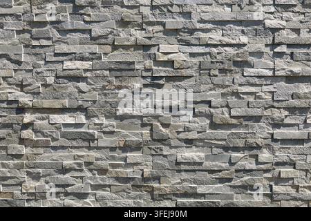 External stone wall covering made of gray quatzite stone strips. Full frame, background and texture. Stock Photo