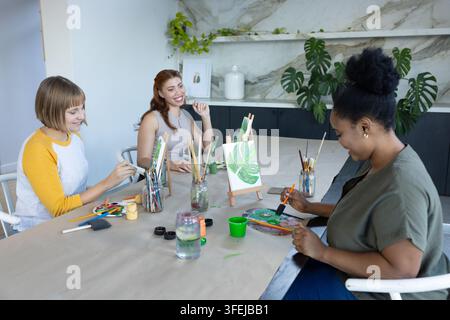 Diverse female friends in casual clothes painting and chatting at art studio with easel, copy space Stock Photo