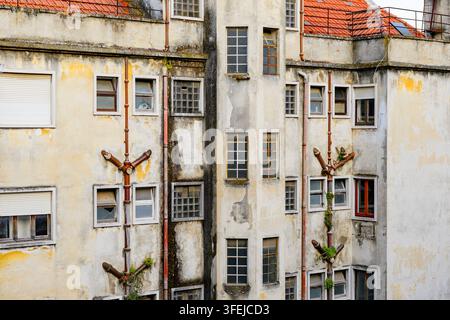 The backsides of old residential buildings in Lisbon. Dilapidated facades, peeling paint, exposed sewer pipes, broken window panes. Stock Photo