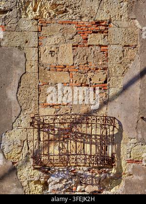 Historic masonry stone and brick wall featuring a rustic, closed wrought iron balcony Stock Photo