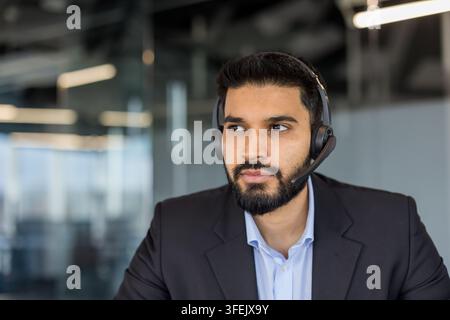 Young indian man wearing a professional headset in an office setting, actively communicating while working in a call center, demonstrating dedicated customer service and technical support Stock Photo