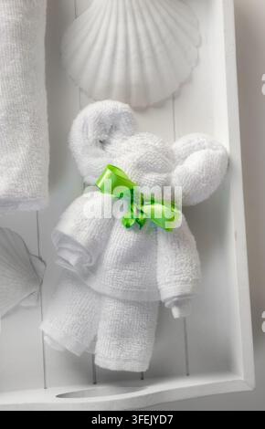 A cute bear-shaped animal folded from a white hand towel, placed on a white tray in a home bathroom. Known as towel origami towel animal. Stock Photo