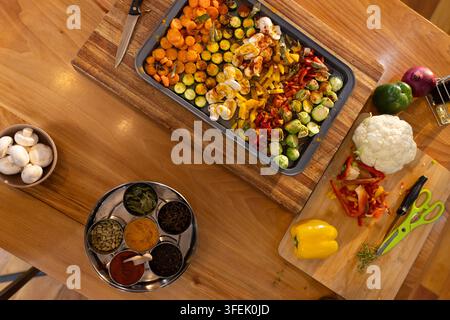 Rectangular metal baking tray is holding sliced vegetables and eggs on wooden table with spice box Stock Photo