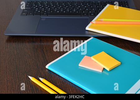 Laptop and Notebooks Arranged on Dark Wooden Table with sticky paper and pencils Stock Photo