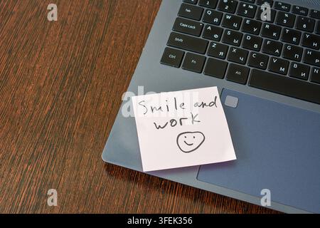 Smile and Work Sticky Note on Laptop Trackpad on wooden desk, copy space Stock Photo