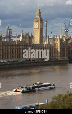 Commuters and tourists ride a boat on London's River Thames, passing the Palace of Westminster and Big Ben to sightsee the UK Parliament. Stock Photo