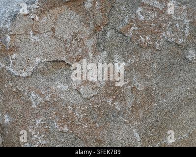Granite boulder surface showing rough geological texture, granular mineral inclusions, white mineral deposits, varicolored natural stone patterns Stock Photo