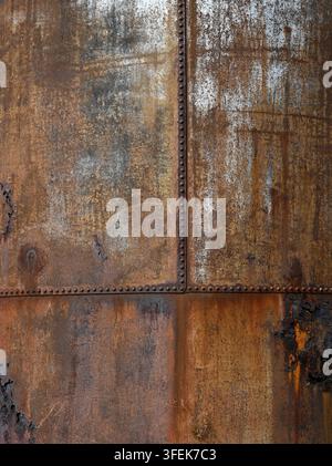 Weather beaten galvanized metal water tank surface with heavy rust coverage, flaking corrosion, rusted bolts and white mineral deposits Stock Photo