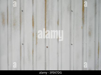 White painted corrugated stippled metal tin surface with dents, scratches, rusty screw heads, worn paint, and exposed yellow areas Stock Photo